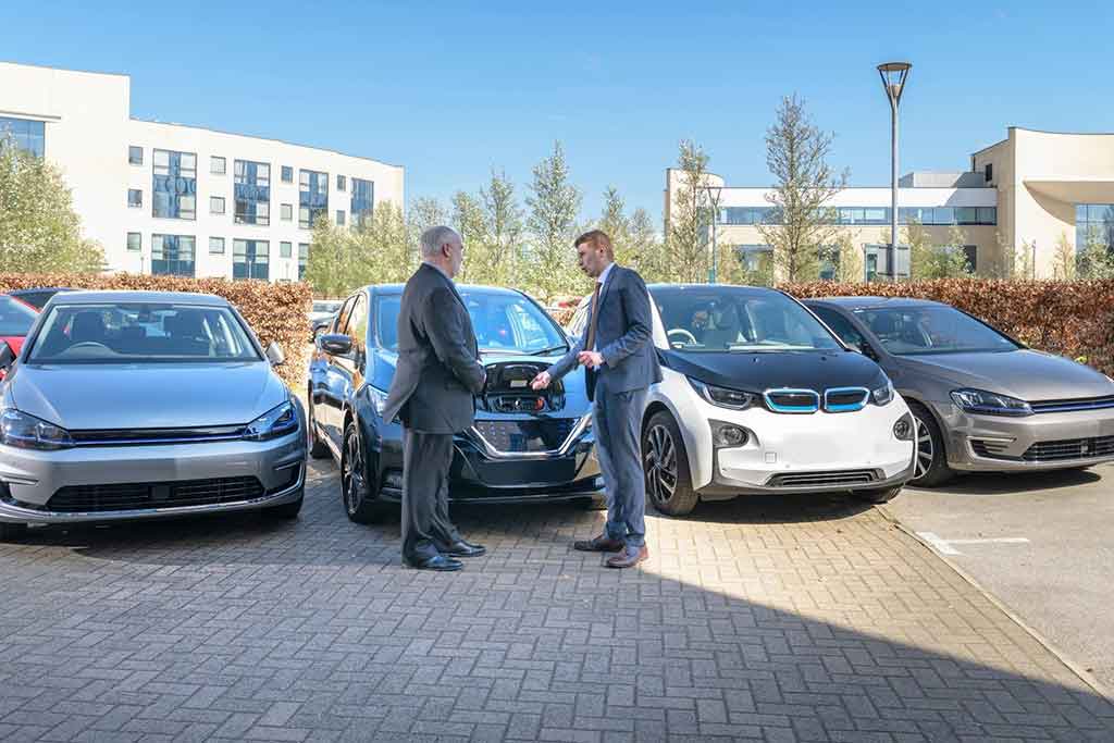 Zwei Geschäftsmäner schütteln sich die Hände vor geparkten Autos