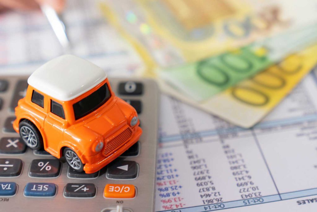 Spielzeugauto auf einem Taschenrechner mit Tabellen und Geld im Hintergrund
