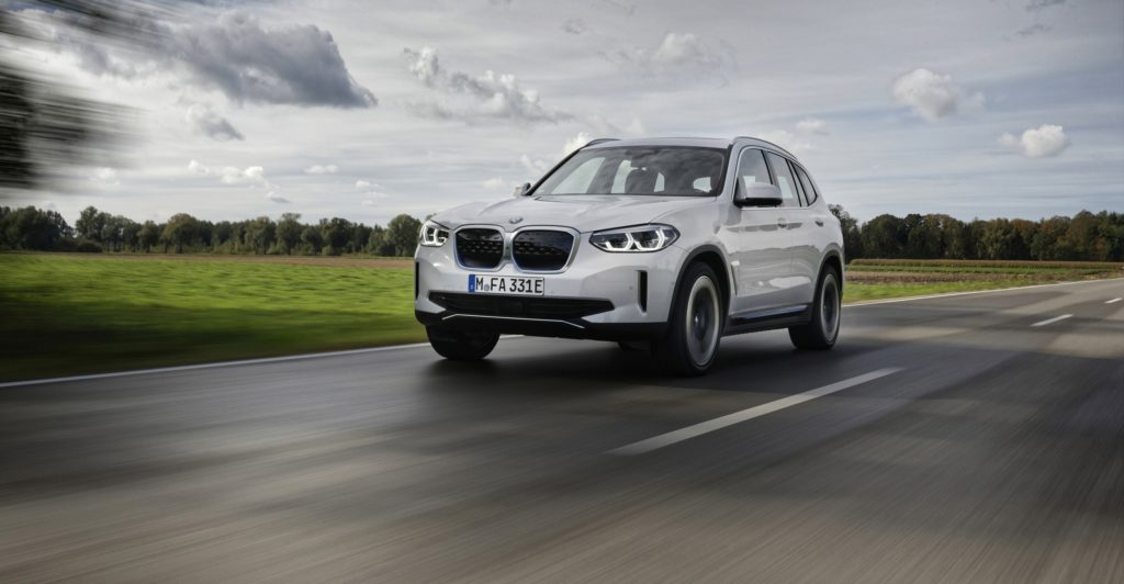 BMW iX3 auf einer Straße mit Wiese im Hintergrund